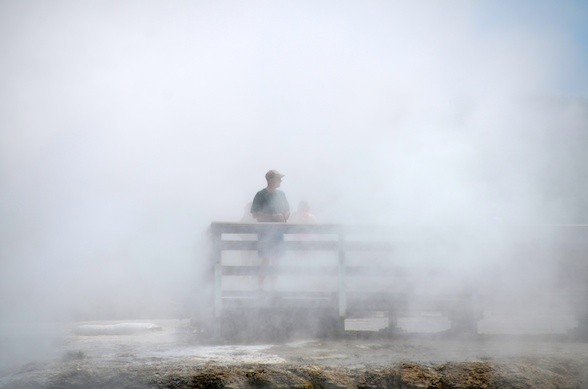 A visitor nearly disappears in steam from the Grand Prismatic
