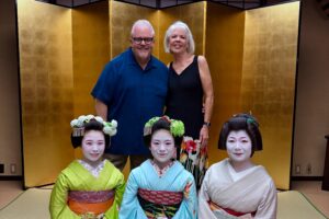 David and Carol with three traditionally dressed geiko and maiko during a private cultural experience in Kyoto, Japan, posed in front of a golden folding screen.