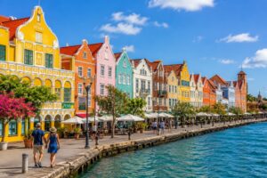 The colorful Dutch colonial waterfront buildings of Willemstad, Curaçao, line the harbor under a bright blue Caribbean sky, showcasing one of the island's most iconic and vibrant landmarks.