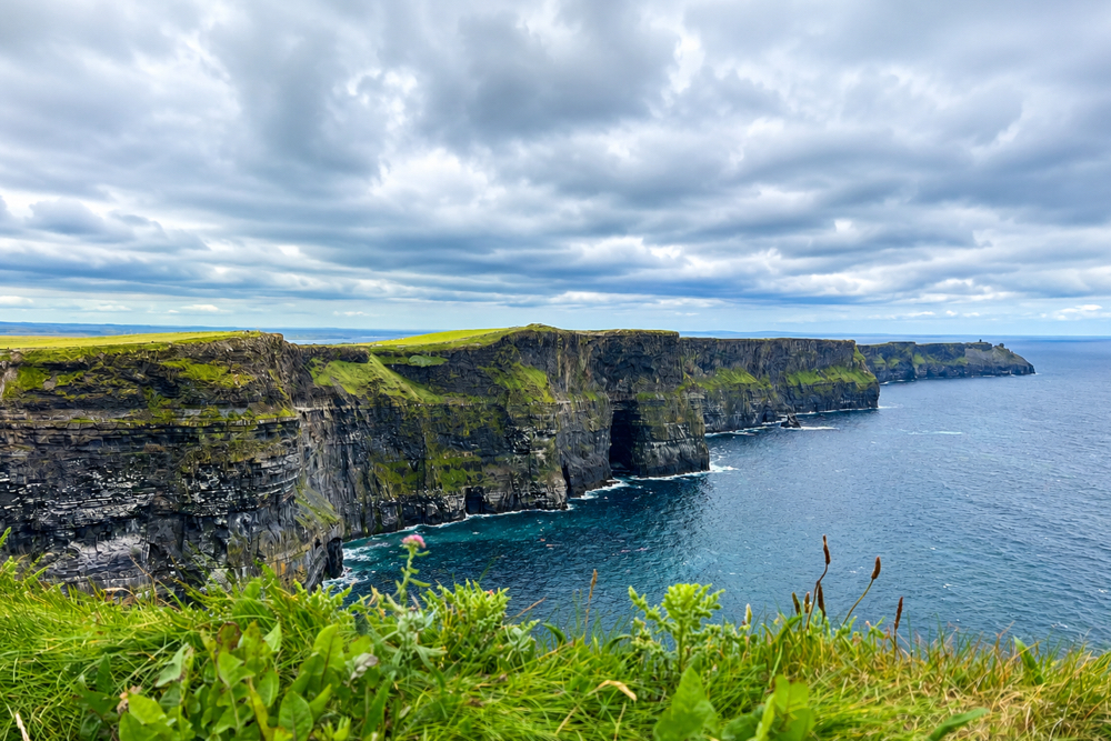 The Cliffs of Moher rise dramatically above the Atlantic Ocean along Ireland's rugged west coast on a windy summer day.