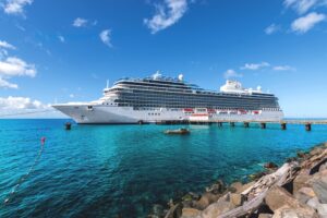 Oceania Cruises' Vista docked in the crystal-clear turquoise waters of the Caribbean, showcasing the luxury cruise ship against a bright tropical sky.